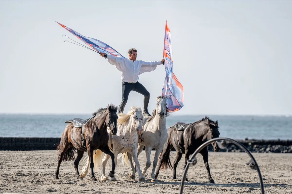 Reiter mit Fahnen auf vier Pferden am Strand